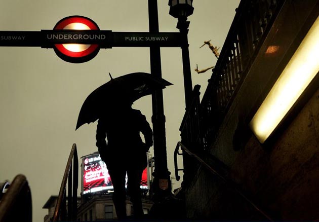 A pedestrian emerges in silhouette from a tube station on a wet day