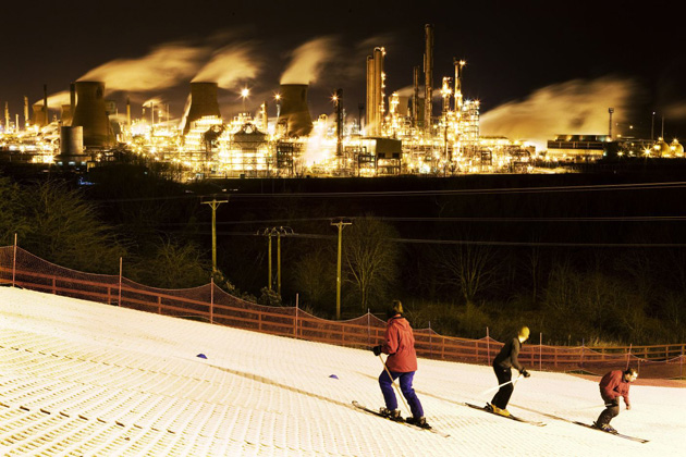 Skiers descend Polmont artificial ski slope run by Falkirk District Council against a back drop of BP's Grangemouth oil refinery