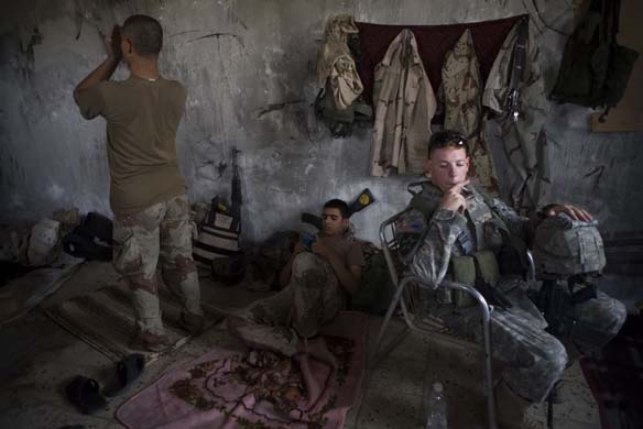 Baghdad, Iraq. An American soldier attached to Stryker units and Iraqi soldiers at an Iraqi Army post in Amiriya, a Sunni neighbourhood in west Baghdad allegedly controlled by Al Qaida. One Iraqi is praying.