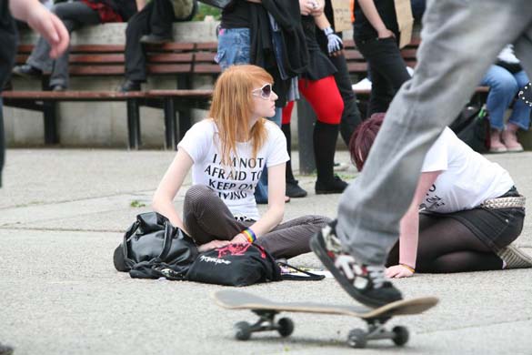 Emo demonstrators sitting on the pavement, skateboarding