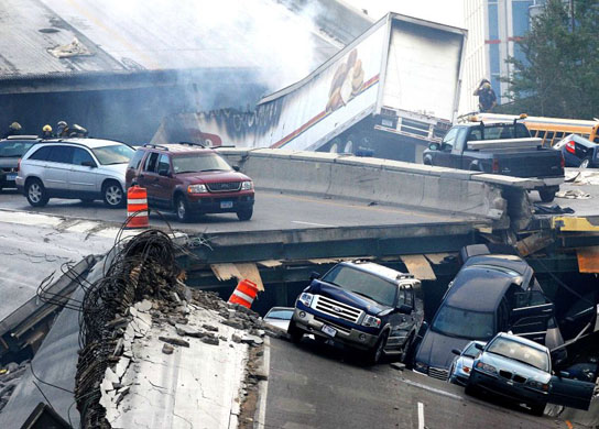 Vehicles are scattered along the broken remains of the bridge