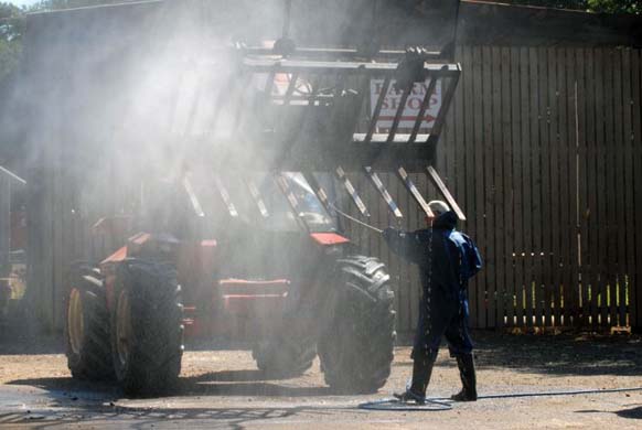 A contractor cleans farm machinery under the watch of a government vet 