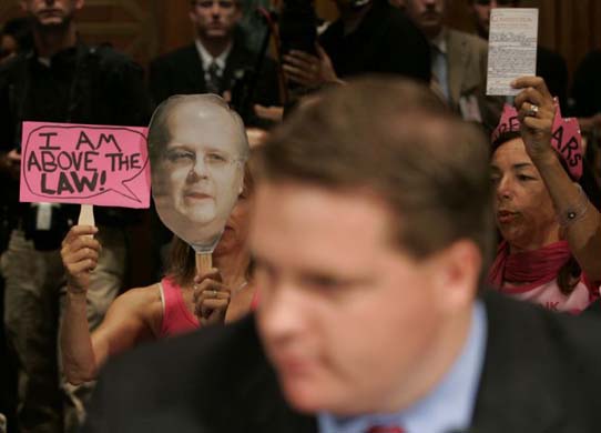Protesters hold up signs including a picture of Karl Rove