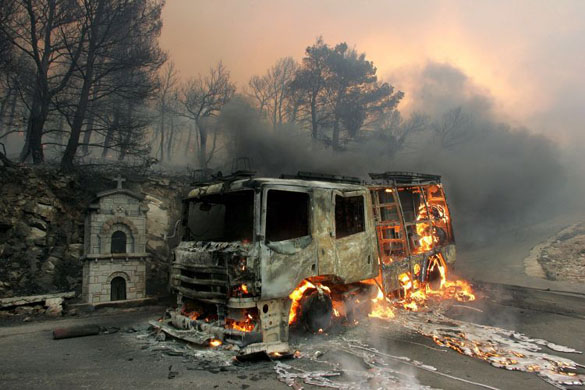 A fire engine burns near a wildfire on Penteli mountain