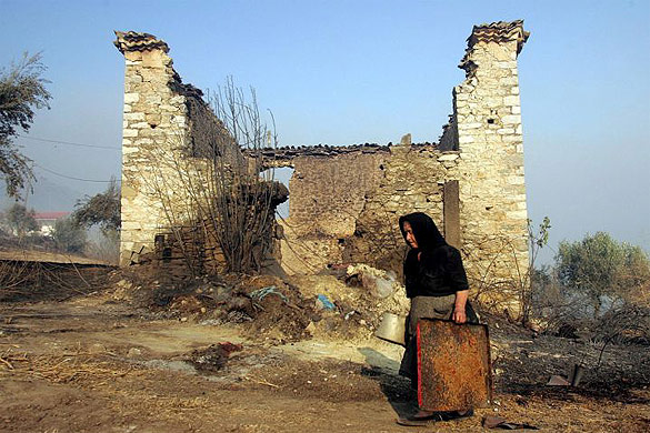 A woman collects belongings from the ruins of her burnt-out house in the village of Platiana, near ancient Olympia