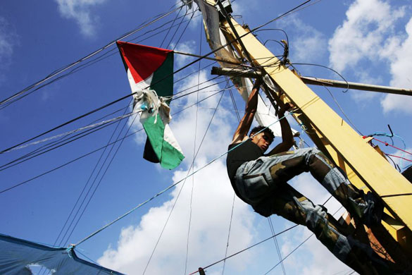 A man fixes a Palestinian flag on an electricity pole