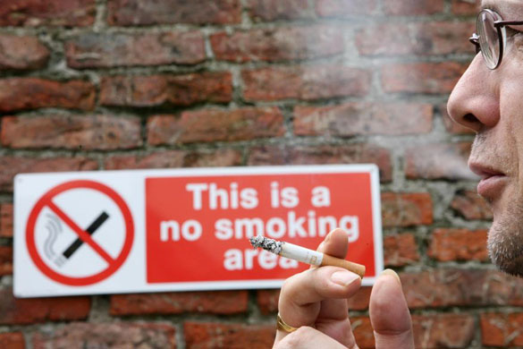 A man smoking a cigarette next to a no-smoking sign