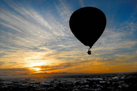 A hot air balloon piloted drifts across the city during an early morning flight
