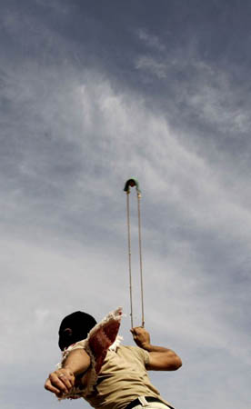 A masked Palestinian demonstrator uses a sling-shot to throw stones
