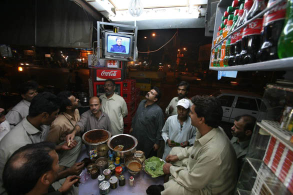 People listen to a televised speech by general Pervez Musharraf in Lahore