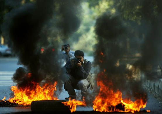 A photographer takes picture of burning tyres set alight by protesters in Islamabad