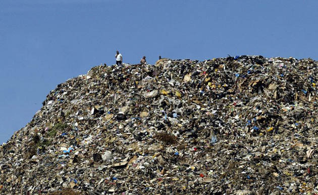 Men stand on top of a mountain of garbage