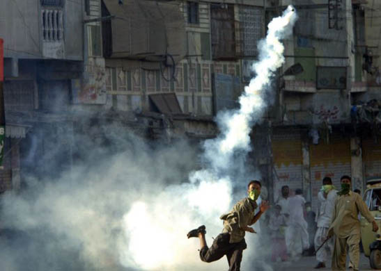 A supporter of Benazir Bhutto's Pakistan People's Party throws back a tear gas shell towards police