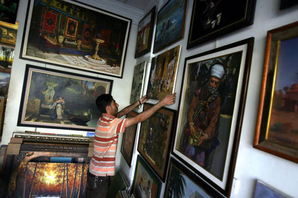 Hussein Abdul Muttalib hangs a painting on a wall in his art gallery