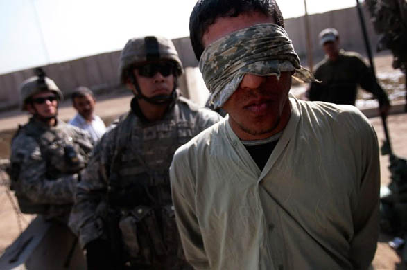 A detained man stands blindfolded
