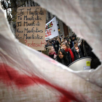 A man holds a banner reading 'I demonstrate, you demonstrate, he demonstrates, we demonstrate, you demonstrate, they demonstrate' as part of a nationwide day of protest