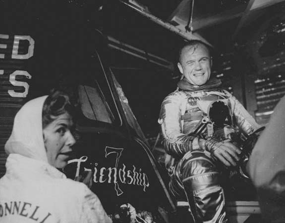 John Glenn sits beside the Friendship 7 capsule