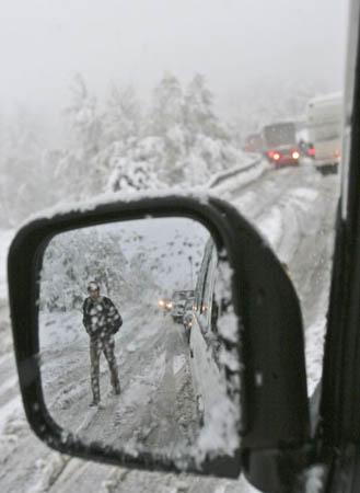 A man walks past a line of traffic which has come to a halt after heavy snow fall