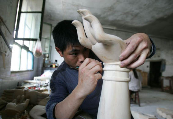 A worker carves a hand of a Buddhist sculpture