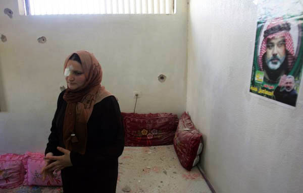 A Palestinian woman stands near a wall in her house which has been pierced by several bullet holes