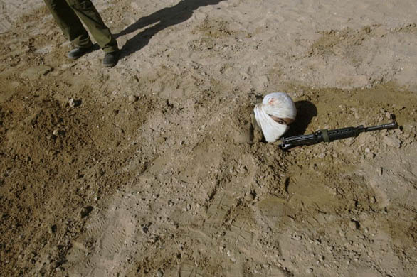 A soldier dressed up as a Palestinian militant is buried in sand during a drill
