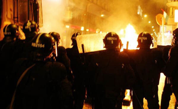 Riot police watch as a Molotov cocktail explodes on a water cannon