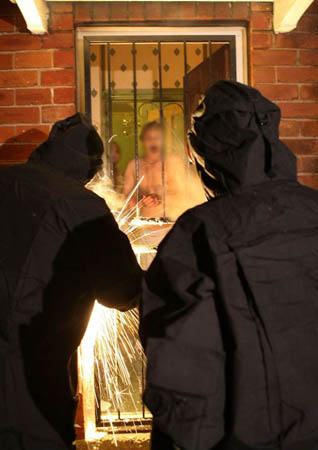 Specially trained police officers use cutting equipment to gain entry to the fortified home