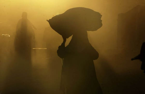 A woman carries a sack on her head as she walks down a street
