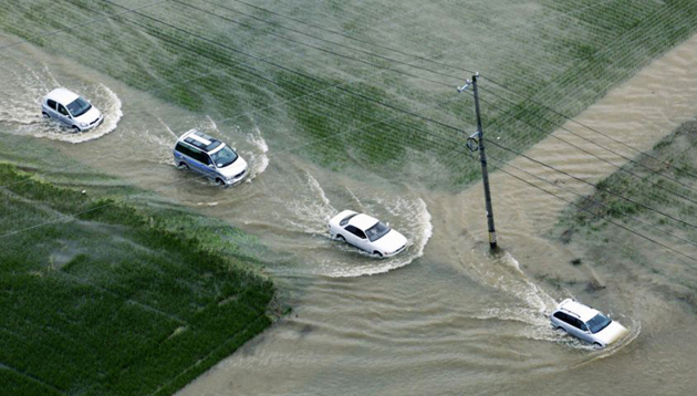 Cars travel down a flooded street between fields in Japan