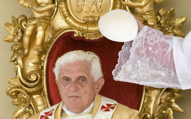 An aide places Pope Benedict XVI's skull cap on his head during a Mass