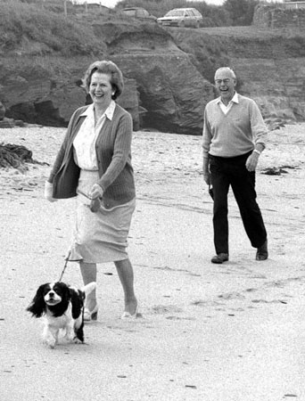 1986, Cornwall, UK: Margaret Thatcher and husband Denis take their holiday host's King Chales Spaniel for a walk along the beach at Constantine Bay