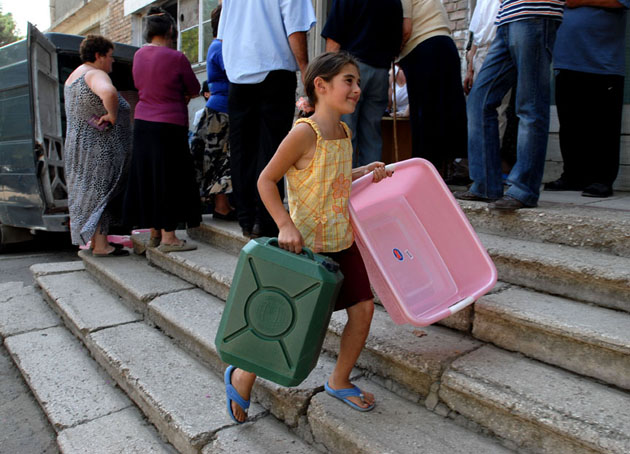 Keti, 8, carries a water container and bowl donated by Save the Children