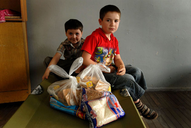 Gocha, 6, and Demuri, 8, sit on a bed with food relief supplies