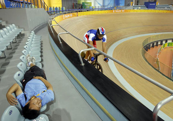A stadium worker takes a nap as a cyclist warms up at the Laoshan Velodrome