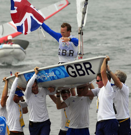 Paul Goodison is lifted high in his boat by team manager Stephen Park and fellow gold medalist Ben Ainslie