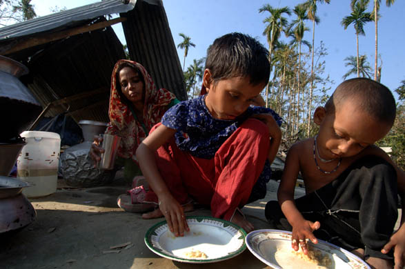 Children eat a meagre meal in a makeshift shelter formed by a panel of