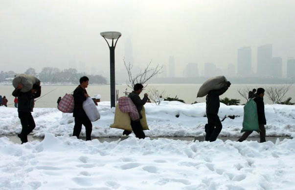 Migrant workers carry items on a snow-covered road