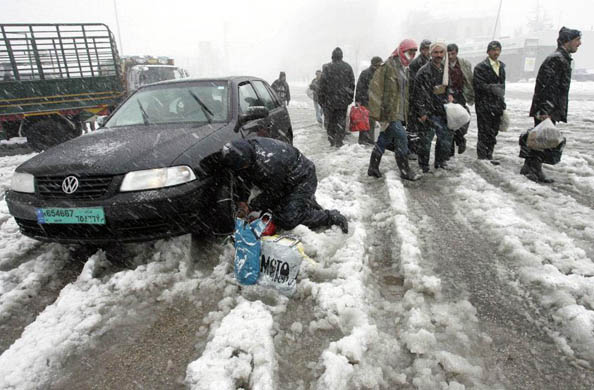 A man fixes a metal chain around his tyres as Syrian workers walk through snow