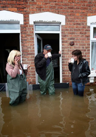 Coyeta Brown, Claus Pittaway and Sophie Pittaway have a cup of tea in flooded Alney Terrace in Gloucester