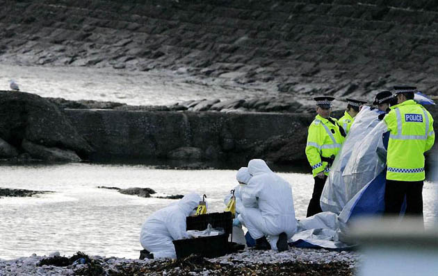 Angus, UK: Police officers shield forensic officers on Arbroath beach, where the severed head of a woman has been found