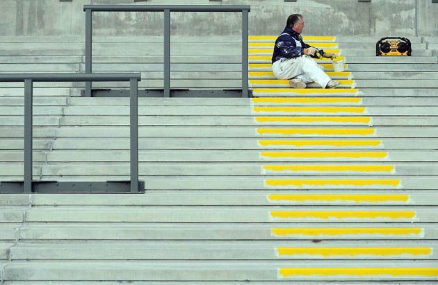 Liverpool, UK: A workman paints yellow stripes on spectator terracing at Aintree racecourse