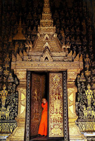 Luang Prabang, Laos: A Buddhist monk stands in front of temple at Wat Xieng Thong