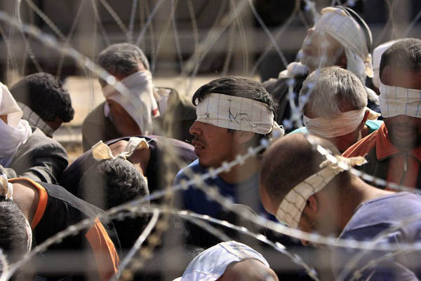 Israel Gaza border: Handcuffed and blindfolded Palestinian prisoners sit on the ground after they were brought out of the Gaza Strip by the Israeli army