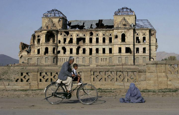 An Afghan woman begs for alms, as a man rides past, infront of the Darul Aman's palace which was destroyed during the 1992 civil war