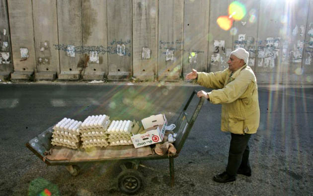 Abu Mohammed, 75, pushes his cart as he sells eggs next to a section of Israel's separation barrier 