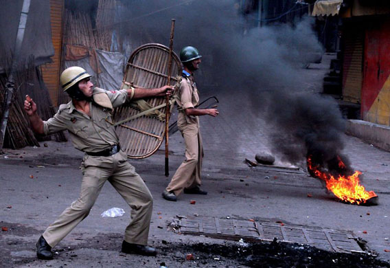 Jammu, India: A policeman throws back stones at protesters during a violent demonstration