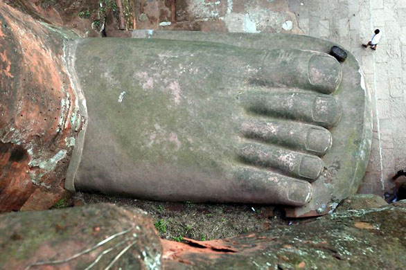 Leshan, China: A tourist walks beside one of the feet of the Grand Buddha