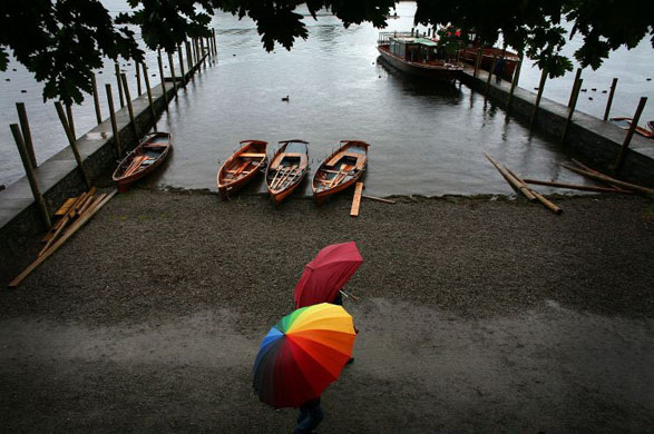 Keswick, UK: Holiday makers protect themselves from the rain as they walk along the shore of Ullswater