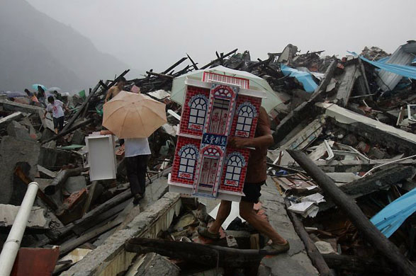 Beichuan County, China: An earthquake survivor carries a paper villa used as an offering to his relatives who died in the Sichuan earthquake