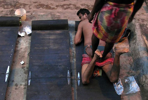 Kolkata, India: A masseur gives massage to a customer on the banks of the river Ganges